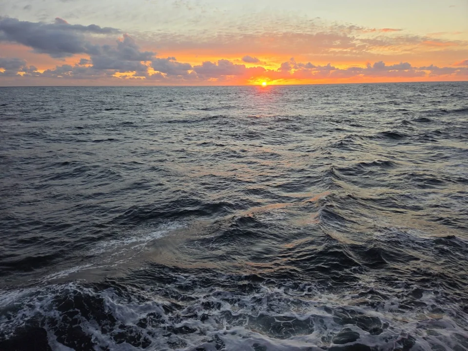 Sun setting over open water and a ship wake.